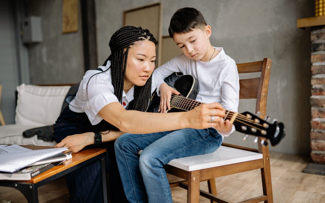 A teacher giving a boy one-on-one private music lessons on the guitar.